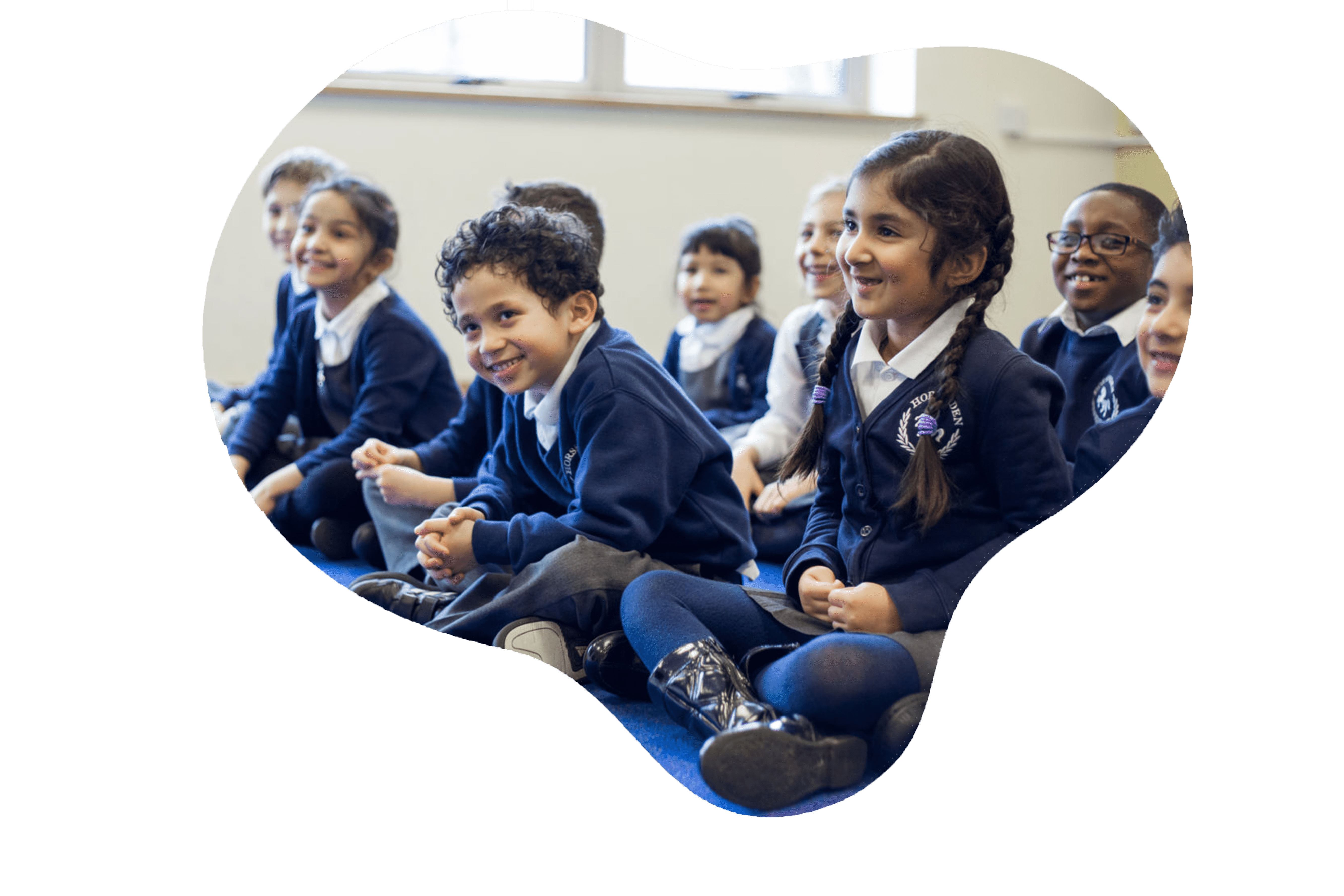 A group of joyful schoolchildren, dressed in blue uniforms, are seated on the floor, their attention seemingly captured by an engaging activity. Their bright smiles and animated expressions convey a sense of excitement and camaraderie, reflecting the lively and positive atmosphere of a classroom environment.