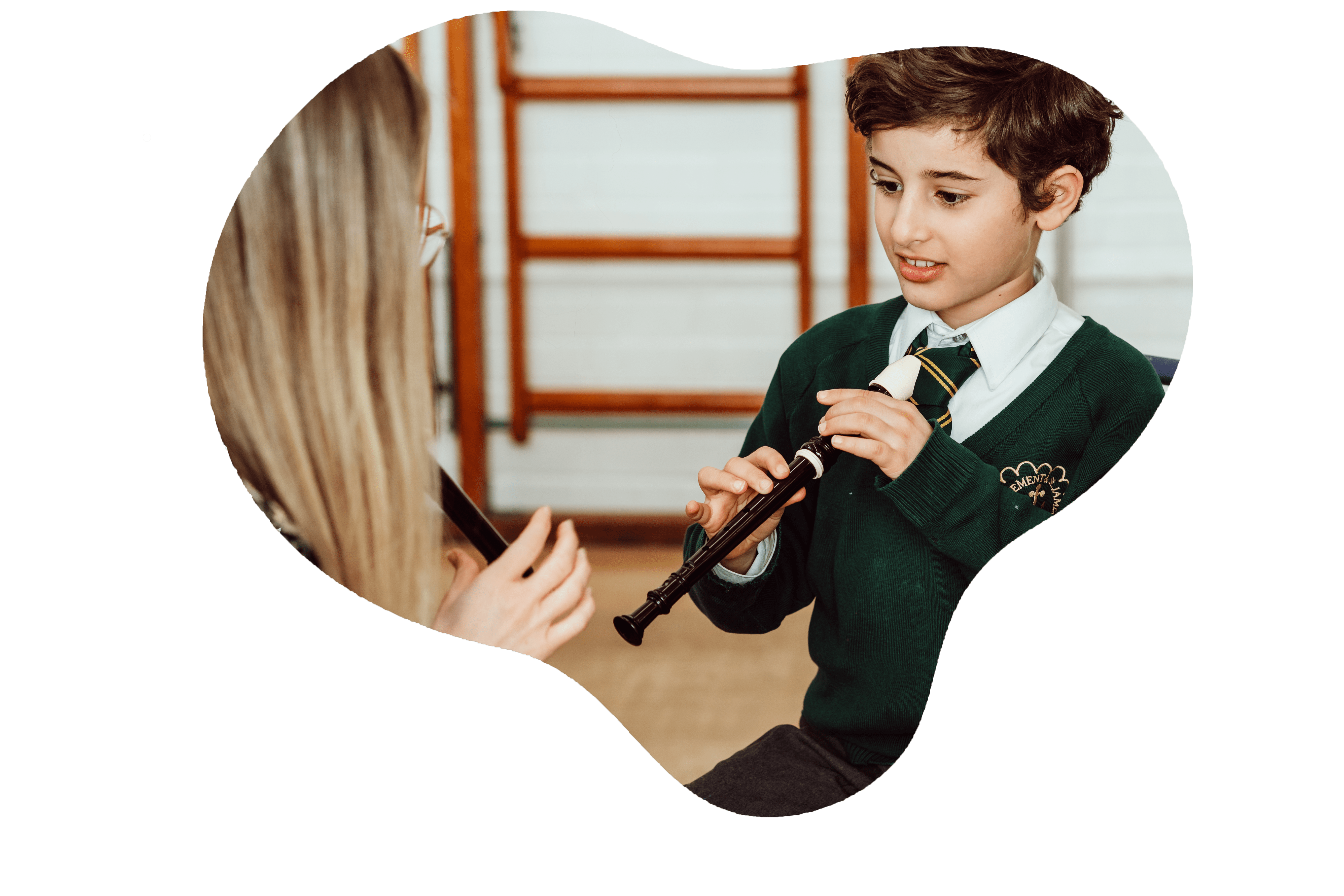A young student in a school uniform is attentively playing a recorder, guided by a partially visible teacher in a classroom setting, reflecting a moment of musical learning and skill development.