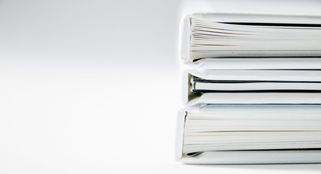 The image shows a stack of hardcover books with white and black spines. The books are placed on their sides, with the pages facing towards the viewer, against a white background, creating a clean and minimalist aesthetic.