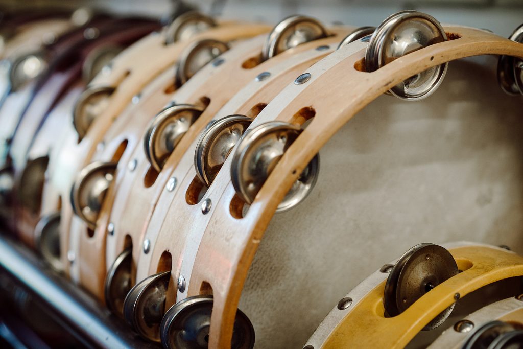 A row of tambourines with wooden frames and metal jingles is neatly arranged, showcasing the instruments' varying shades and sizes, ready for use in a music education setting. The focus on the tambourines' details conveys a sense of preparation for a hands-on, rhythmic learning experience.