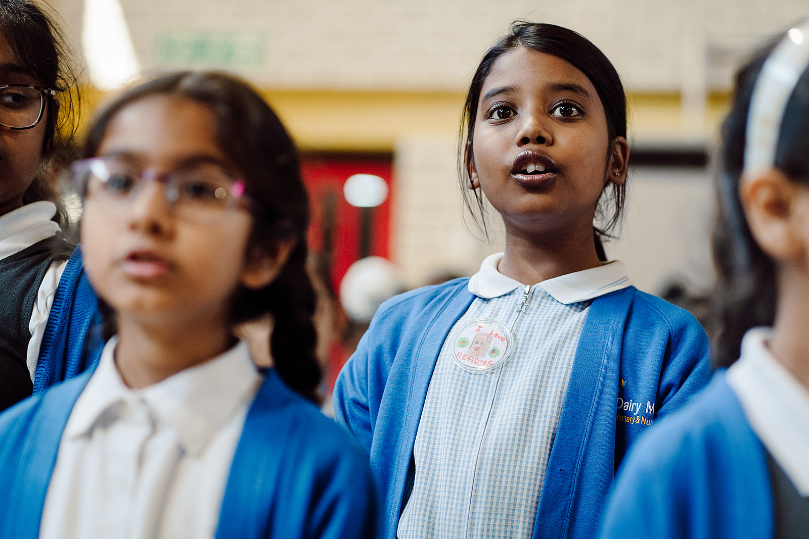 Children wearing a blue school uniform are singing together in an assembly